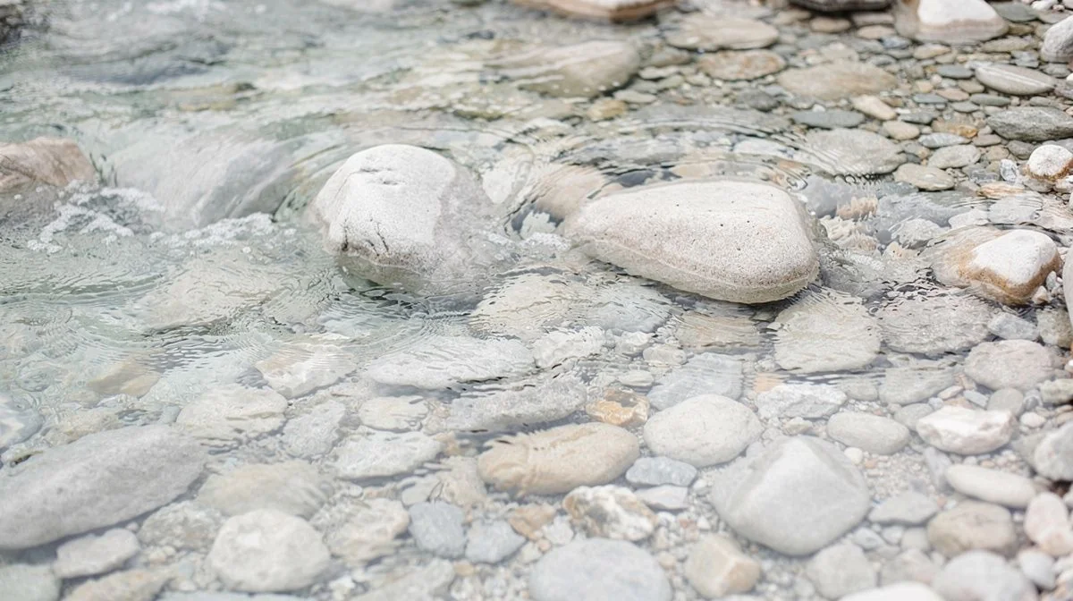 a bright shallow stream running over smooth pale stones in daylight