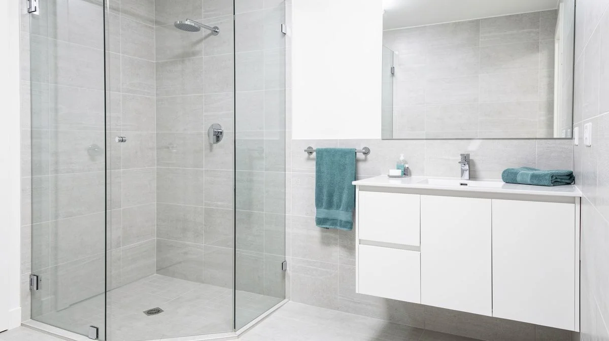 A newly renovated modern bathroom with a tiled walk-in shower, white vanity and teal accents