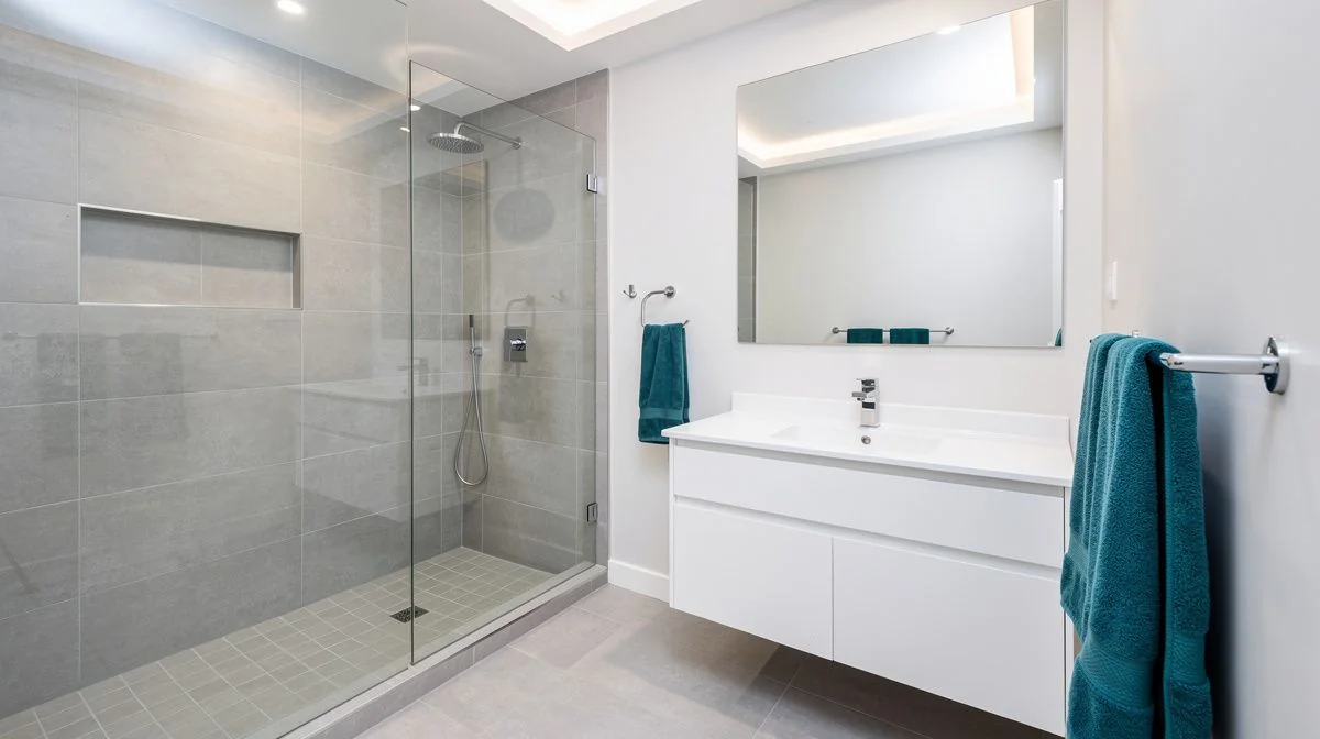 A newly renovated modern bathroom with a tiled walk-in shower, white vanity and teal accents