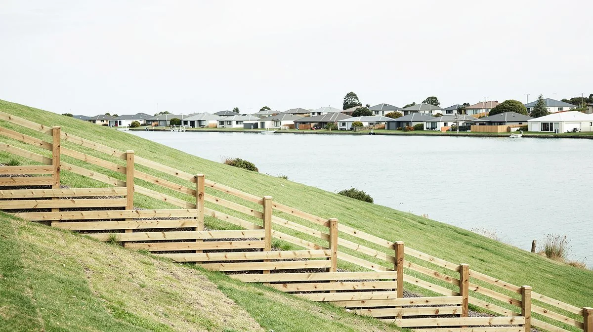 Stepped timber fence following a sloping Porirua hillside boundary with the harbour and a row of suburban roofs in the distance