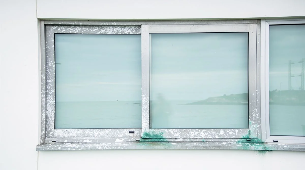 Weathered aluminium window frames showing salt corrosion on a coastal home near the Tauranga harbour