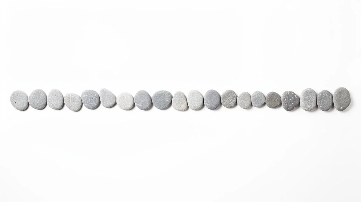A single even row of plain smooth grey pebbles on a bright white surface