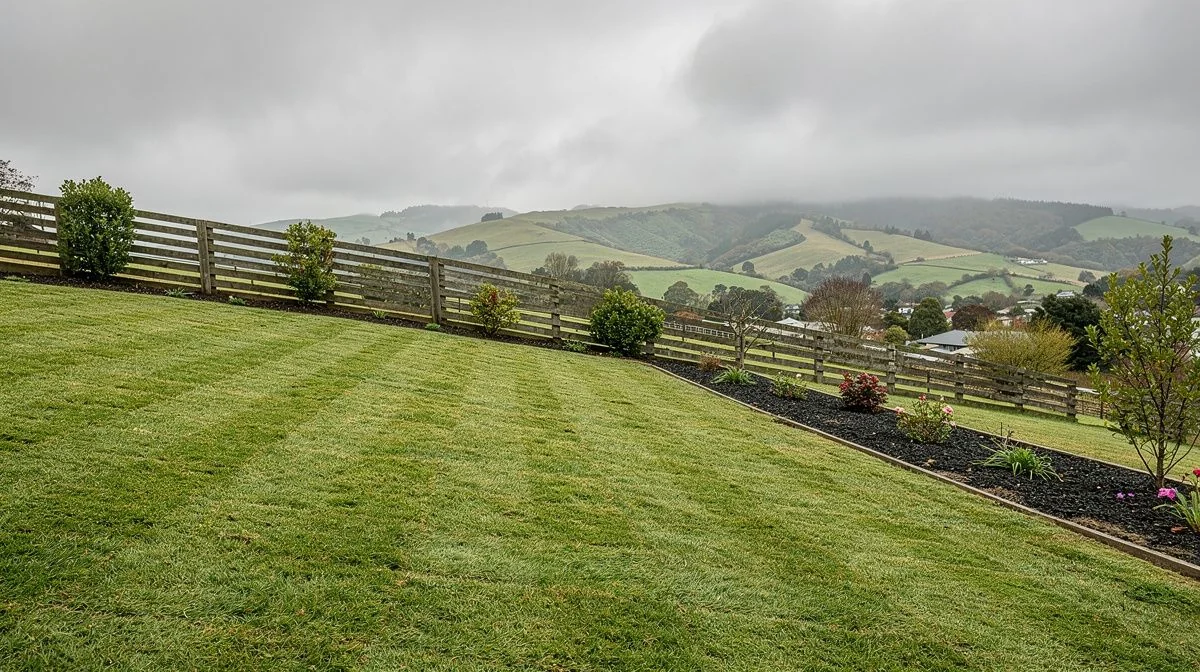 Damp mown lawn on a sloping Lower Hutt section with a timber fence behind