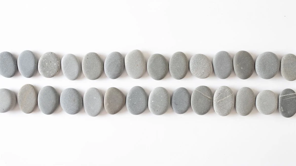 Two neat separate rows of smooth grey pebbles on a bright white surface