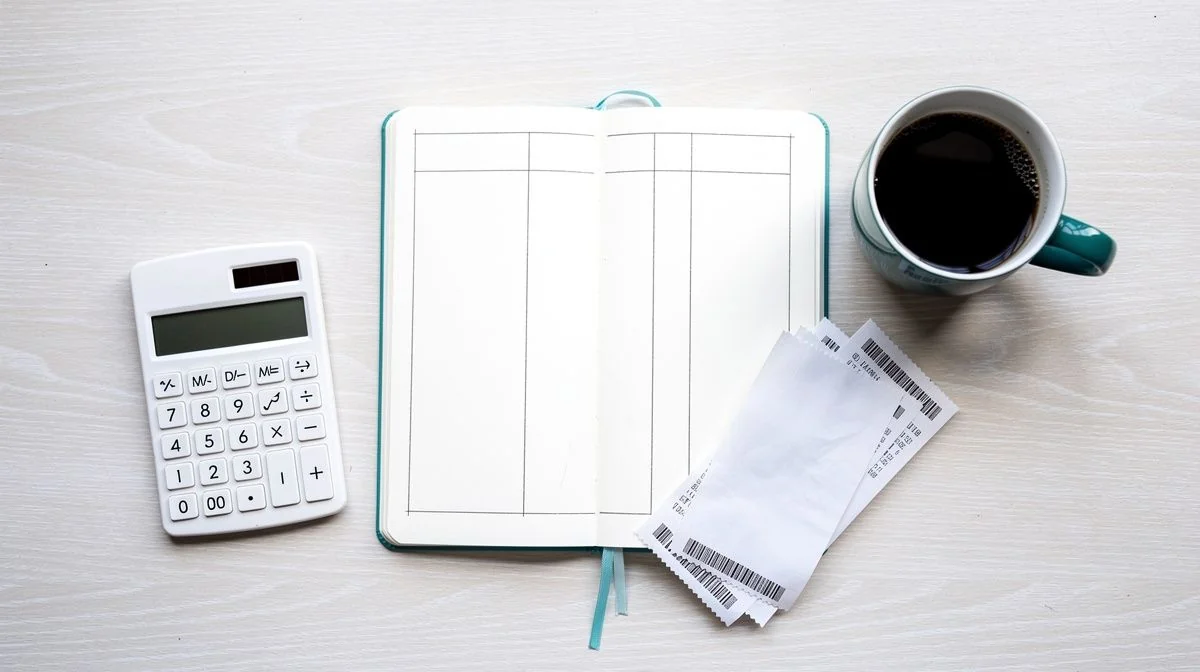 Notebook with three-column budget grid, receipts and calculator on a wooden table