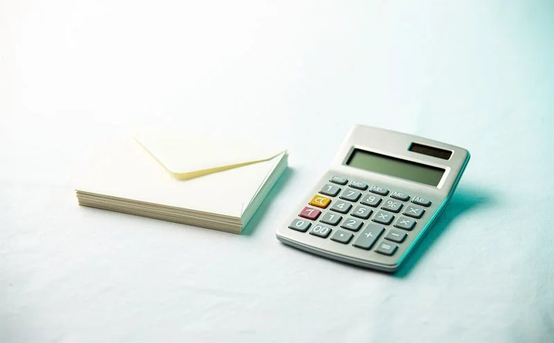 A small brushed steel desk calculator beside a neat stack of blank cream envelopes