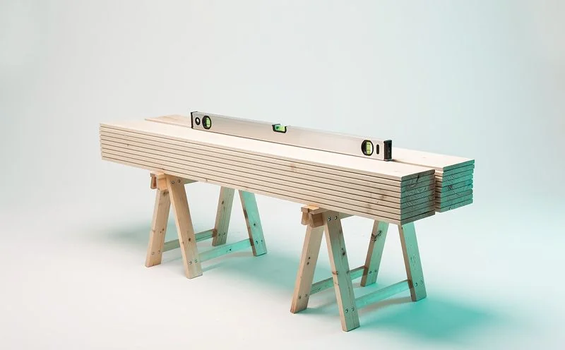 A stack of pale timber planks and a spirit level resting on a timber sawhorse