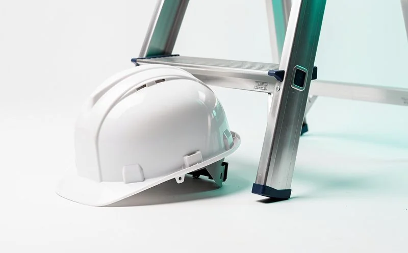 A white safety hard hat resting against a folded aluminium step ladder
