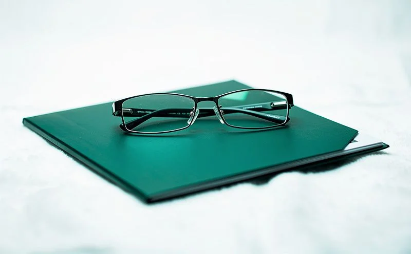 A pair of folded reading glasses resting on a closed dark green document folder