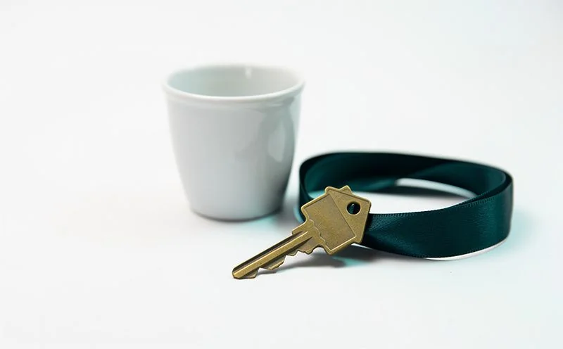 A brass house key on a dark teal ribbon beside a small white ceramic pot