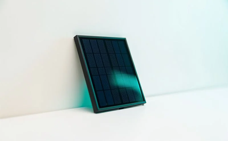 A small dark blue solar panel leaning against a pale wall in low sunlight