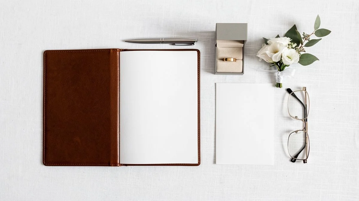 Overhead flat lay of a wedding celebrant kit with a vow booklet, pen, ring box, posy and ceremony card