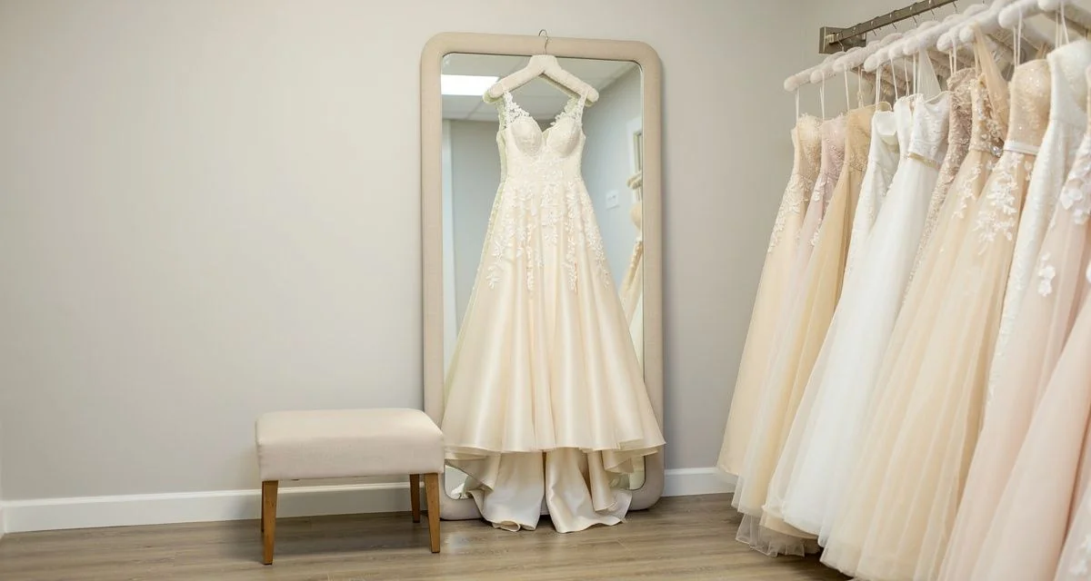 Bridal fitting room with a gown on a hanger beside a mirror and rail of dresses