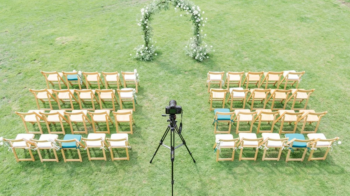 Camera on tripod facing empty outdoor wedding ceremony chairs